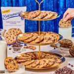 Entenmann's Ready to Bake Cookie Dough - a 3-tiered serving tray full of chocolate chip cookies with a hand dipping a cookie into a glass of milk.