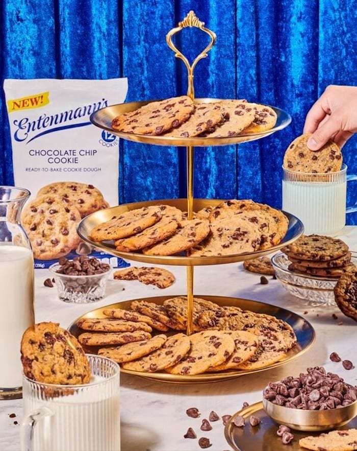 Entenmann's Ready to Bake Cookie Dough - a 3-tiered serving tray full of chocolate chip cookies with a hand dipping a cookie into a glass of milk.